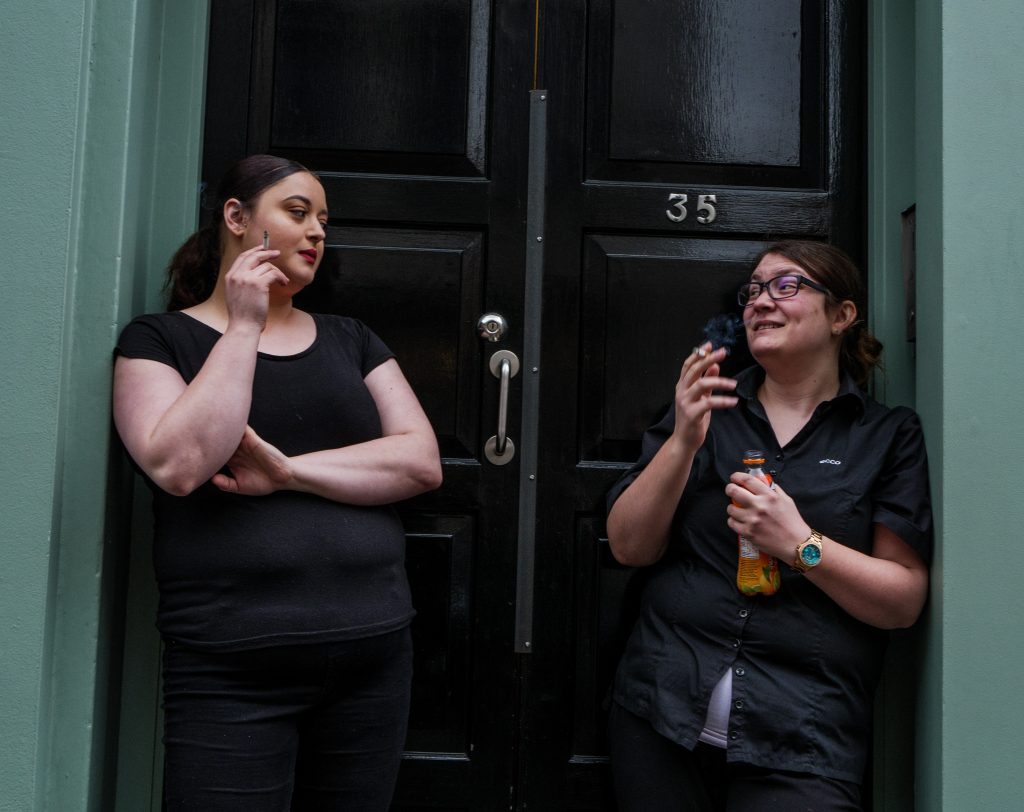 Ladies smoking together outside a door.